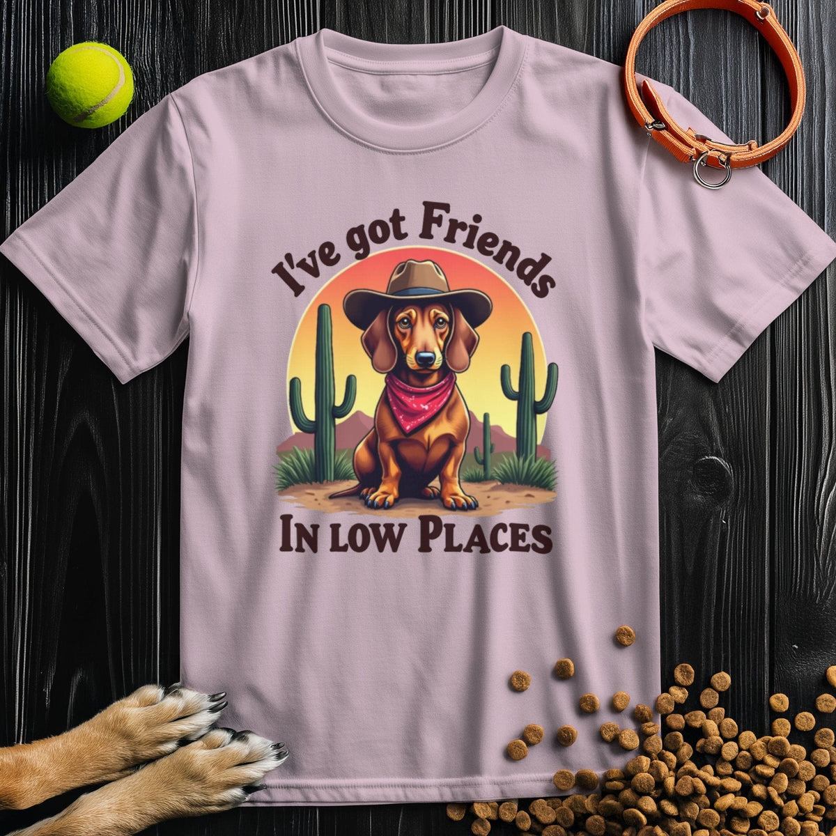 Light pink 'I've Got Friends In Low Places T-Shirt' with a cowboy dachshund print, a playful and stylish pick for dog-loving fashion fans.