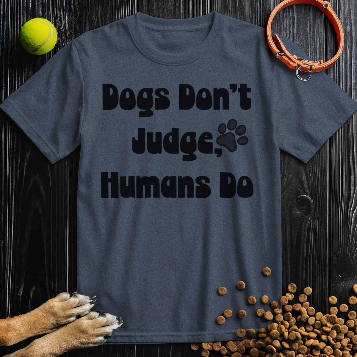 Charcoal gray 'Dogs Don't Judge, Humans Do' dog t-shirt made from ethical cotton, displayed with dog accessories on a dark wood background.
