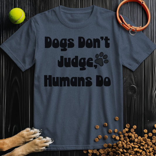 Charcoal gray 'Dogs Don't Judge, Humans Do' dog t-shirt made from ethical cotton, displayed with dog accessories on a dark wood background.