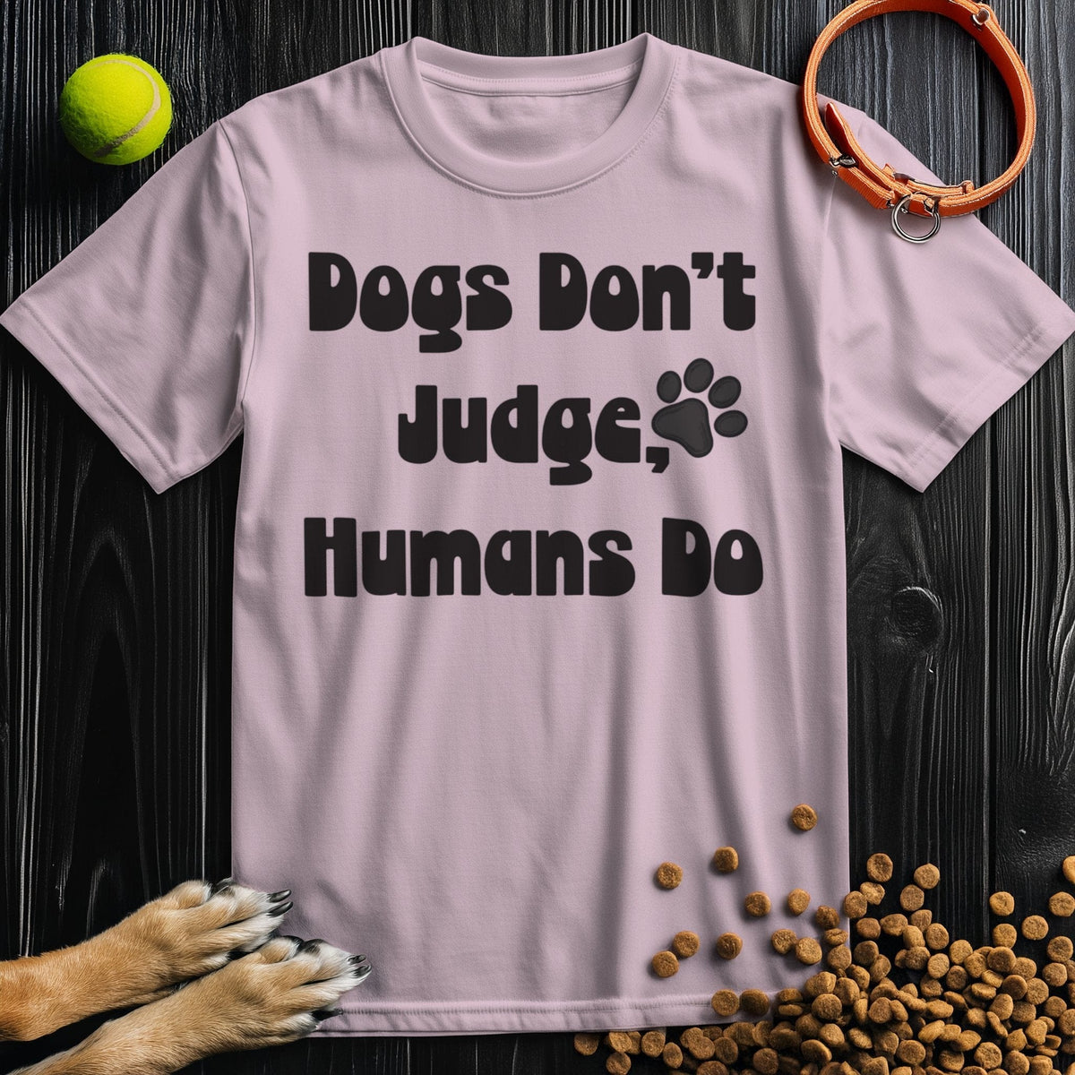 Light pink 'Dogs Don't Judge, Humans Do' t-shirt made from ethical cotton, featuring bold black lettering and a paw print for pet enthusiasts.